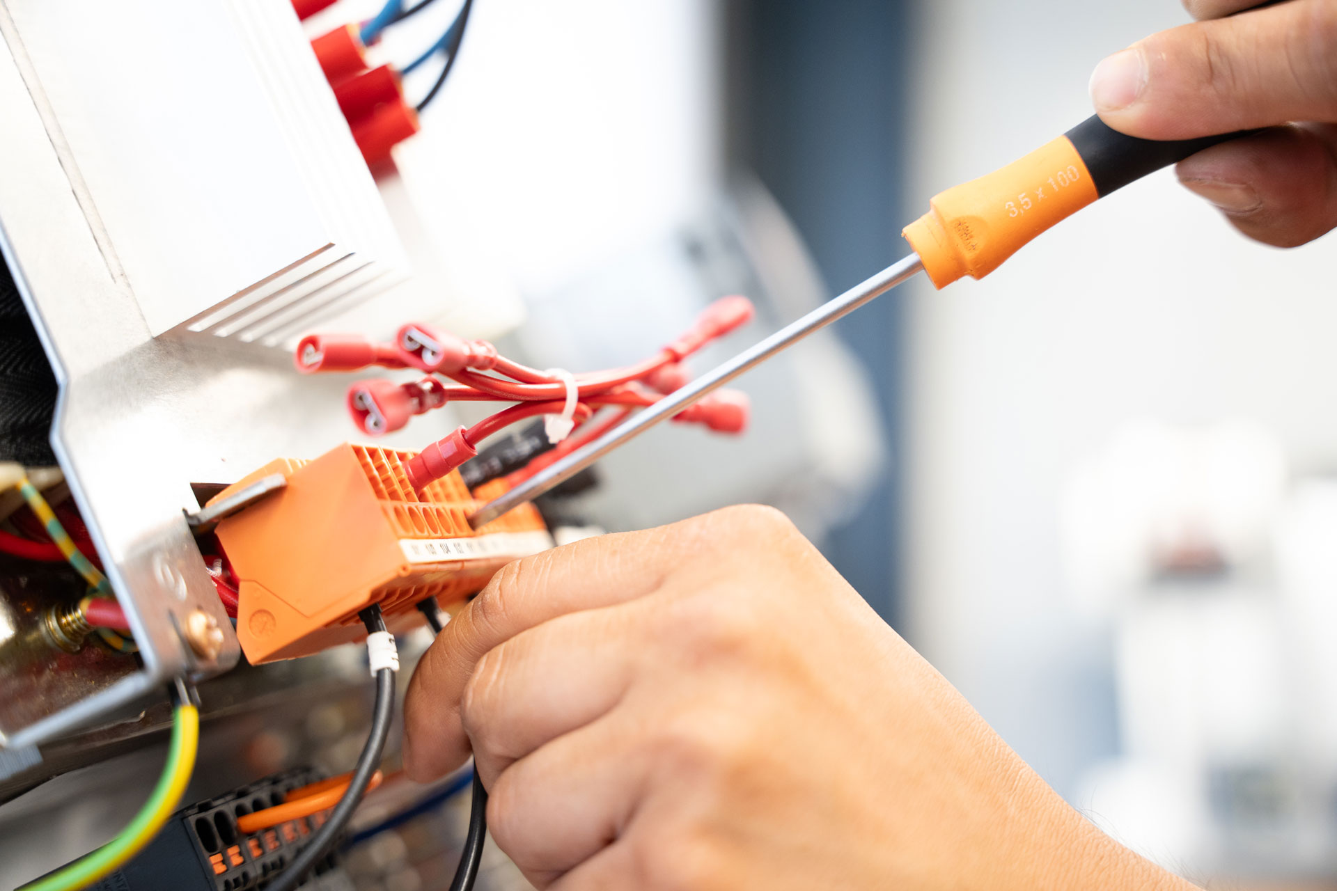 Hände schließen mit einem Schraubendreher Kabel an eine orangefarbene Klemmleiste an