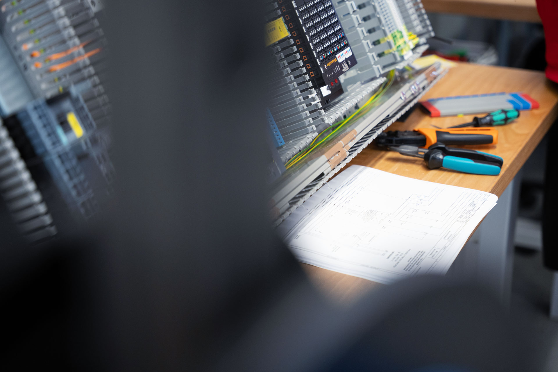 Werkbank mit Schaltplan, Zangen und Schraubendrehern neben einer bestückten Montageplatte