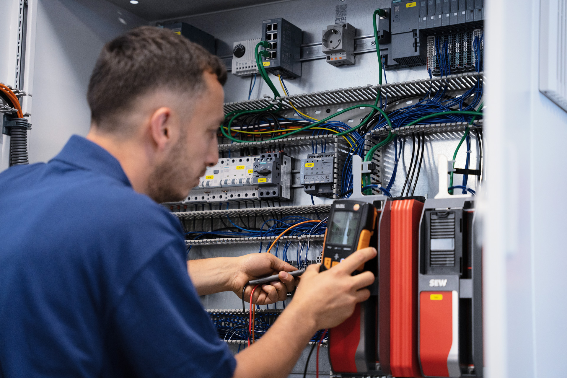Mitarbeiter misst mit einem Multimeter an einem verdrahteten Schaltschrank