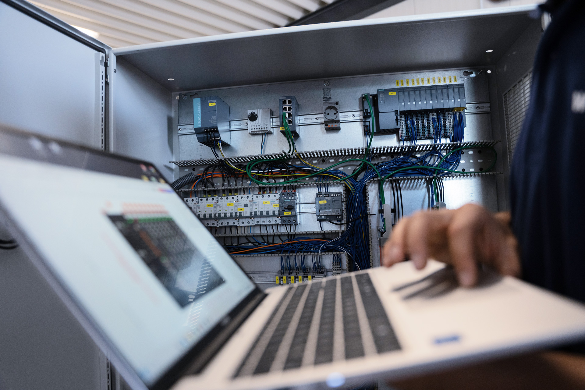 Laptop mit Programmiersoftware vor einem geöffneten, verdrahteten Schaltschrank